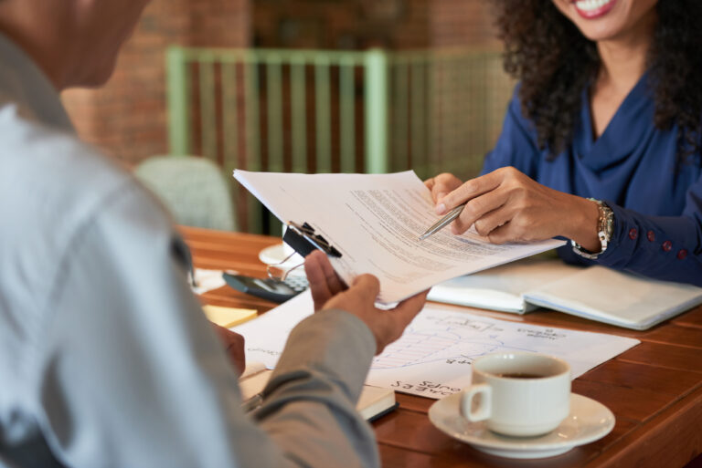 Two individuals discussing legal documents at a table, one holding papers and a pen, with a coffee cup and notes visible, representing client consultation at a law firm in Kingwood.