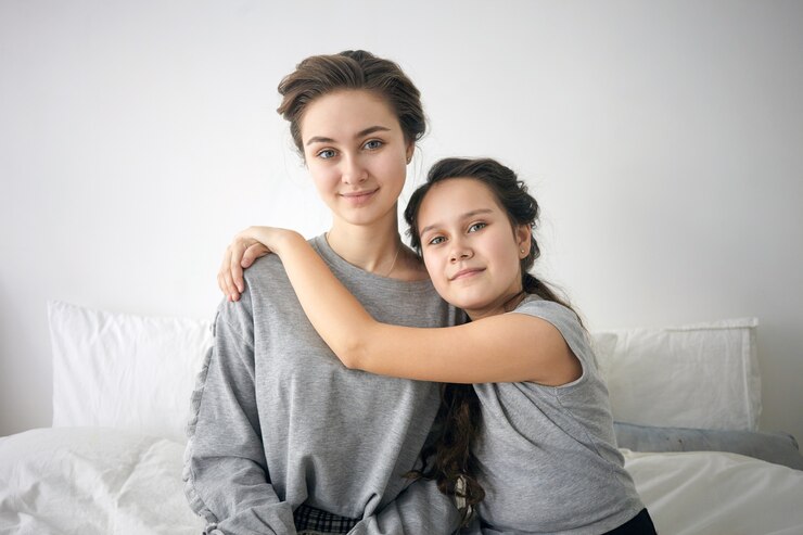 Two girls, one older and one younger, sitting on a bed, smiling and embracing, conveying warmth and familial connection, relevant to child custody and parenting relationships in Texas.
