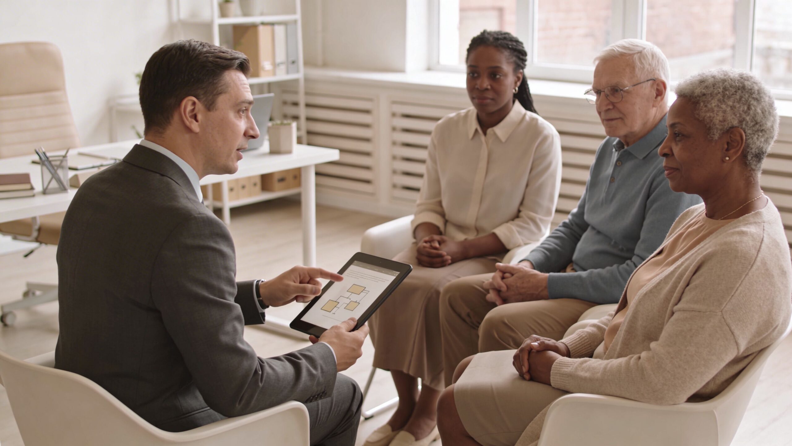 A professional attorney discussing legal estate planning documents on a tablet with an elderly couple in office.